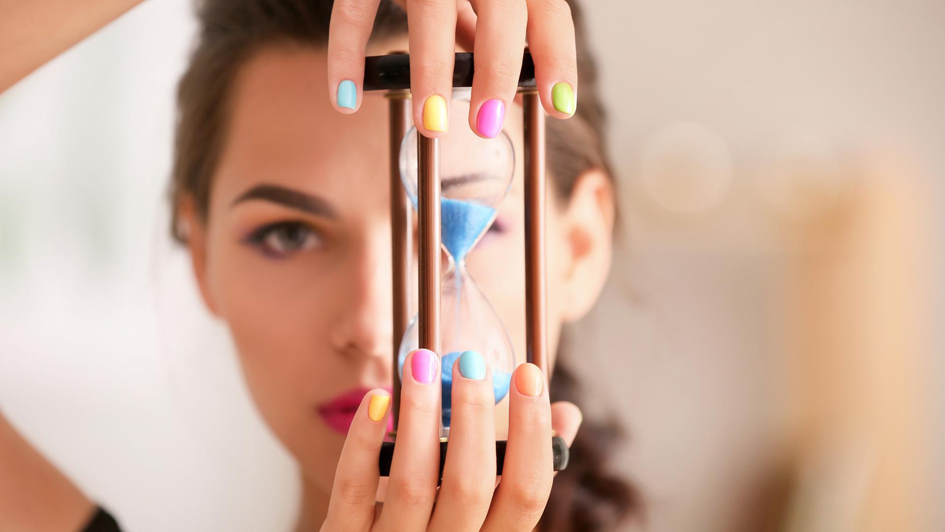 Young woman with colourful manicure holding hourglass