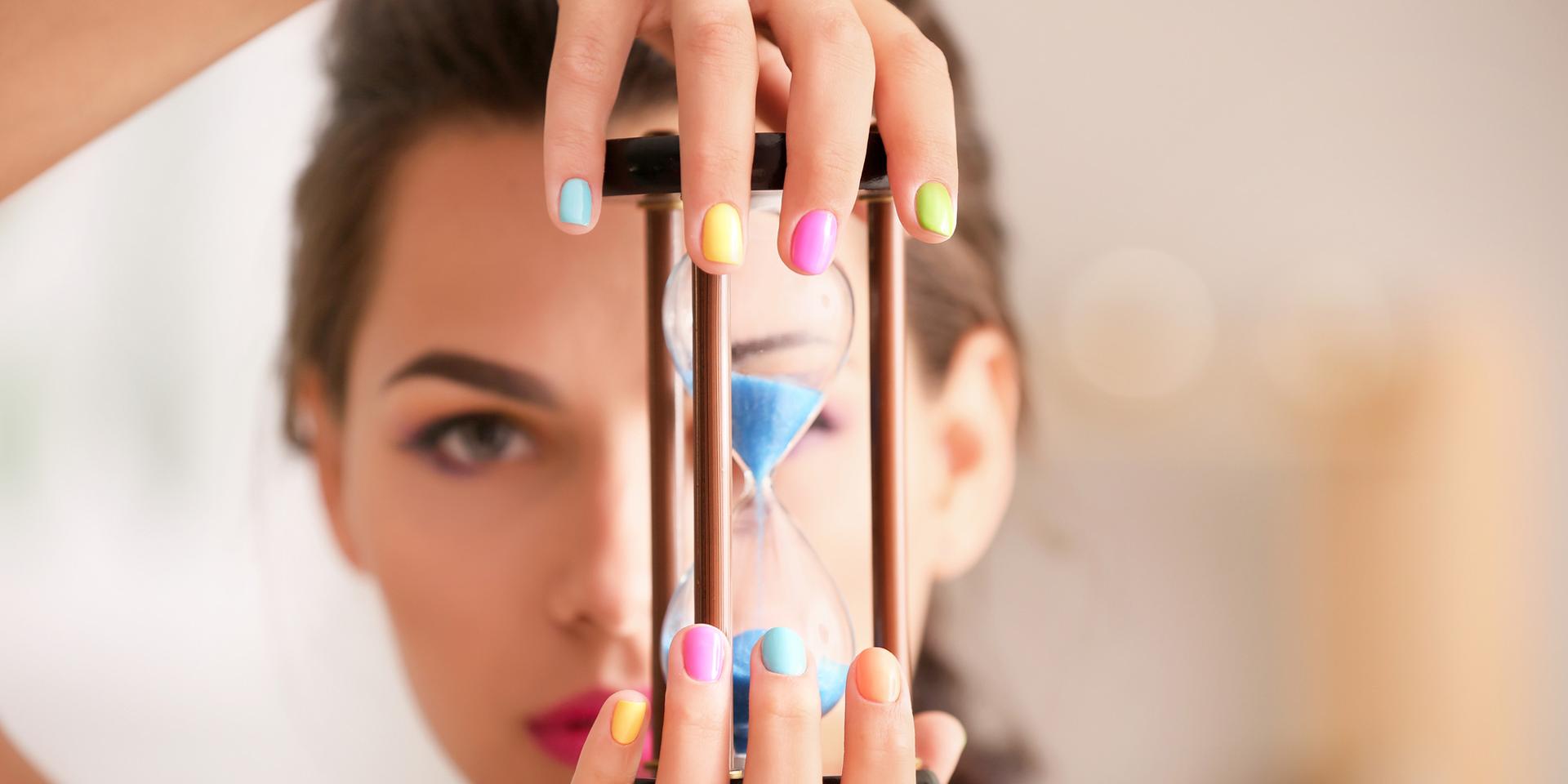 Young woman with colourful manicure holding hourglass