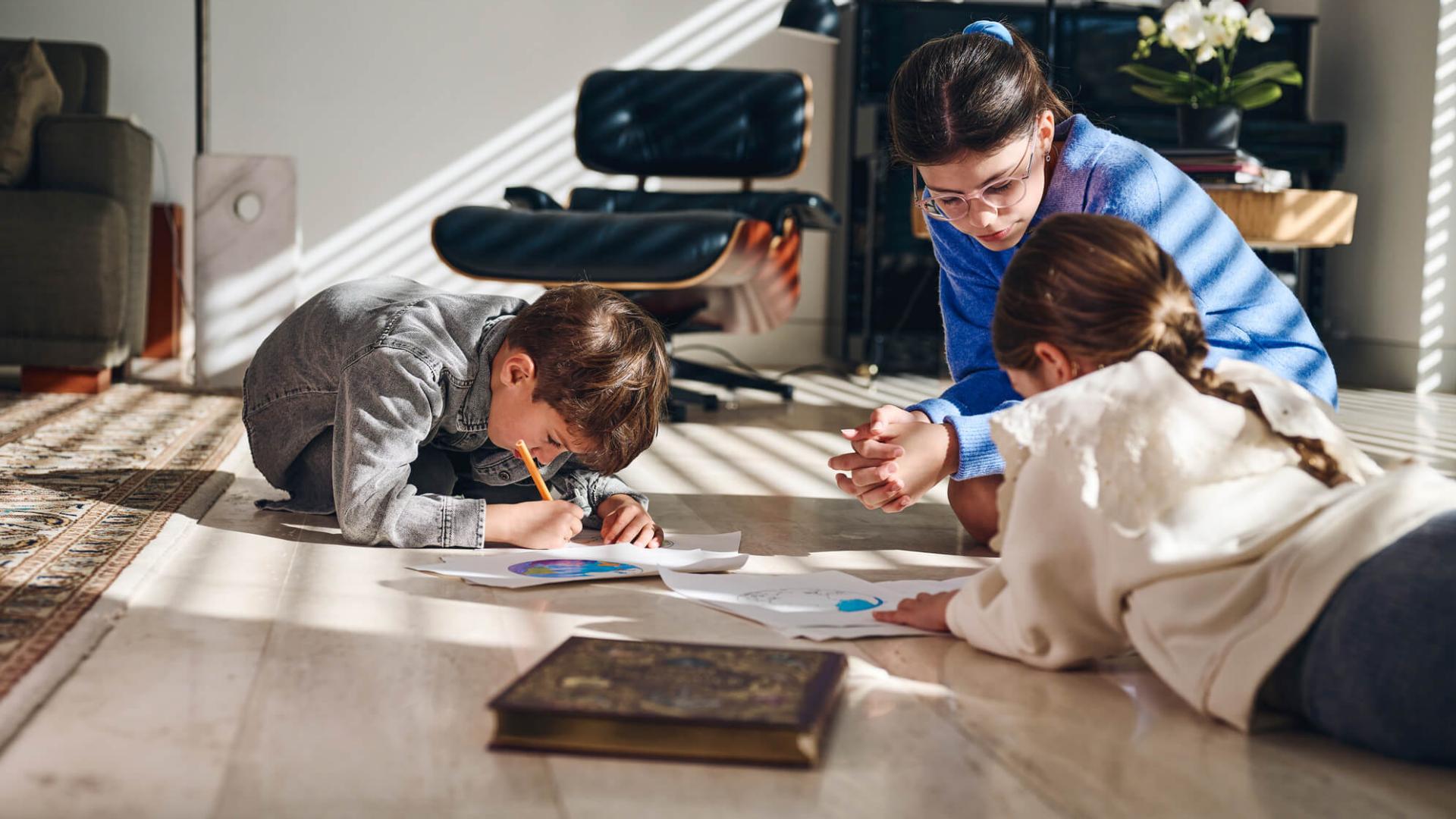 Children drawing on the floor, holding their eyes close to the paper. 