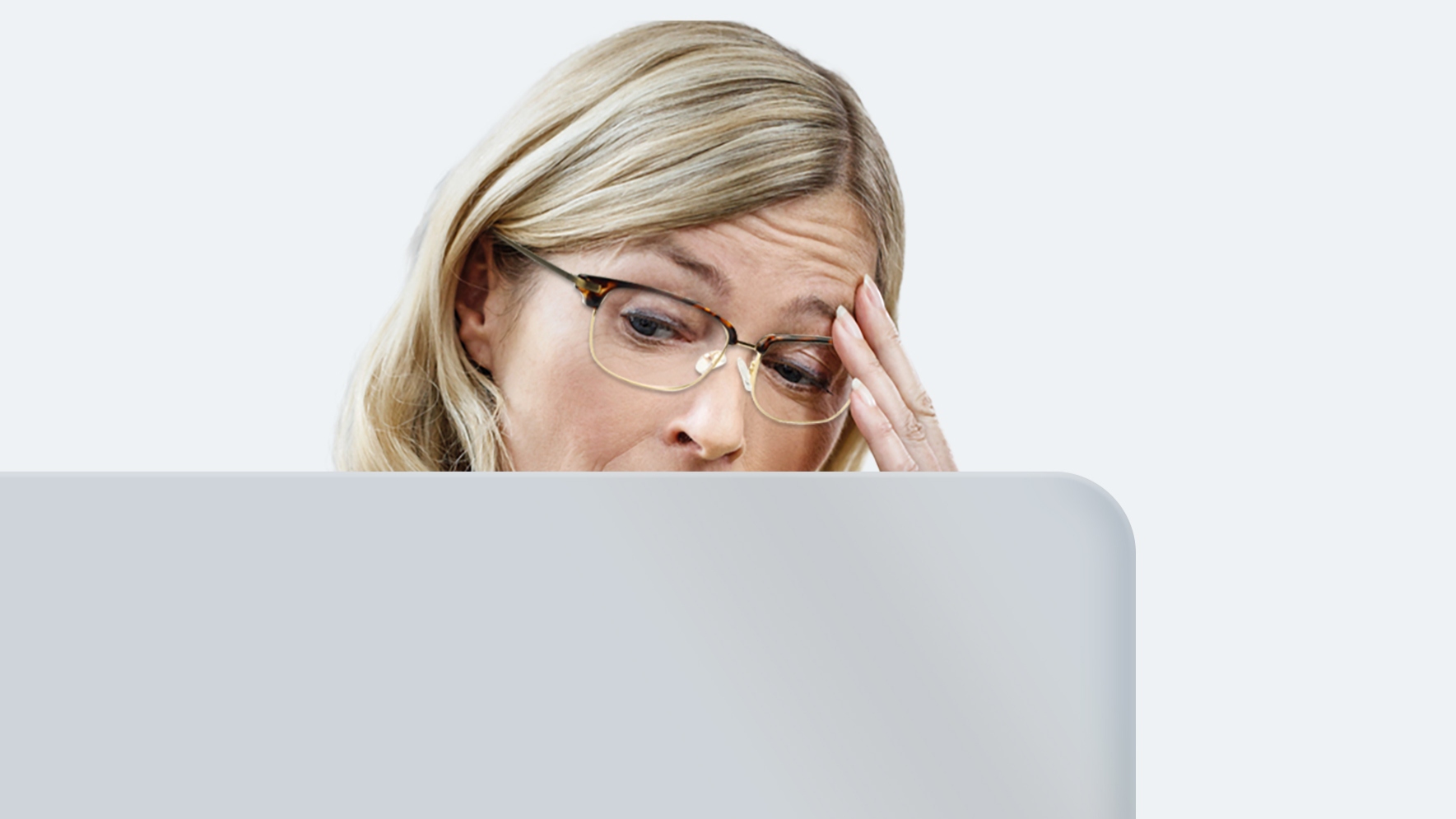 A middle-aged woman with long blonde hair wearing distance glasses is experiencing eye strain because her lenses are not made for staring at a screen all day.